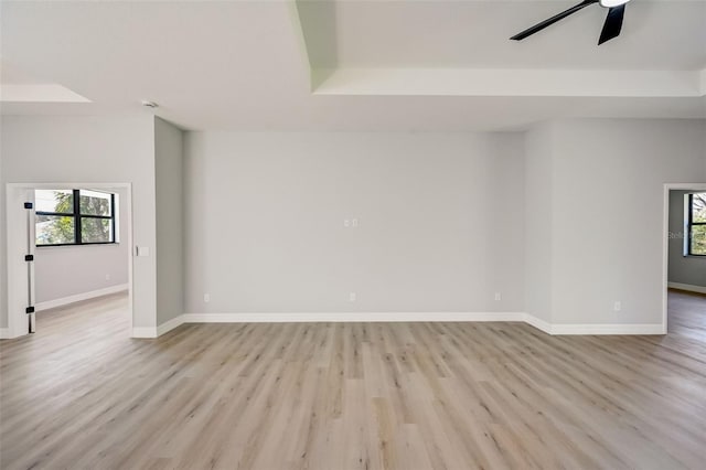 empty room with ceiling fan, plenty of natural light, light hardwood / wood-style floors, and a tray ceiling