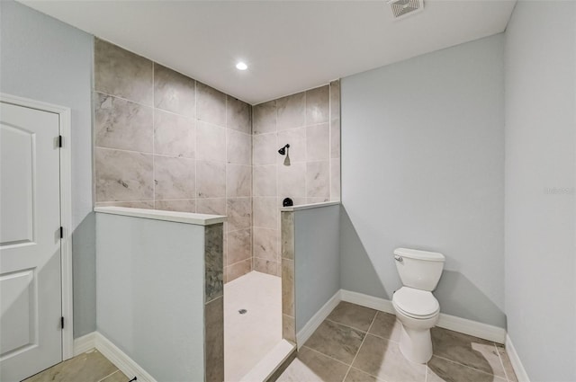 bathroom with tiled shower, toilet, and tile patterned flooring