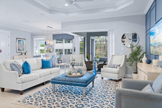 living room featuring ceiling fan with notable chandelier, crown molding, and a raised ceiling