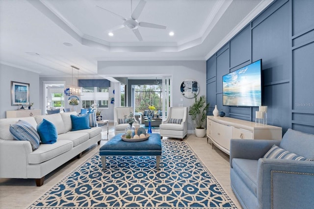 living room featuring ceiling fan with notable chandelier, a tray ceiling, and crown molding