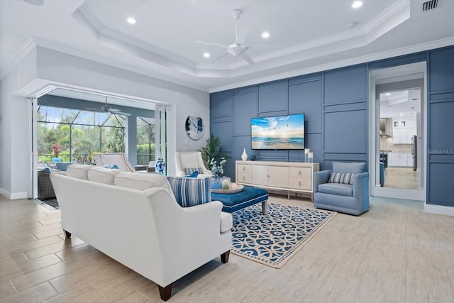 living room with ceiling fan, a raised ceiling, and crown molding