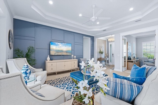 tiled living room with ceiling fan, a raised ceiling, and ornamental molding