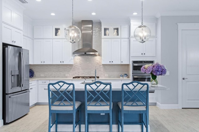 kitchen featuring an island with sink, white cabinetry, wall chimney range hood, and stainless steel appliances