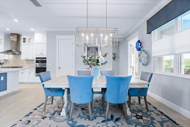 dining area with light hardwood / wood-style floors, crown molding, and an inviting chandelier