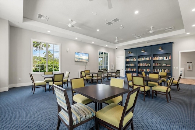 dining room featuring ceiling fan, a raised ceiling, and dark colored carpet