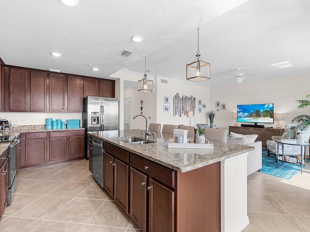 kitchen with appliances with stainless steel finishes, decorative light fixtures, sink, a kitchen island with sink, and light stone counters