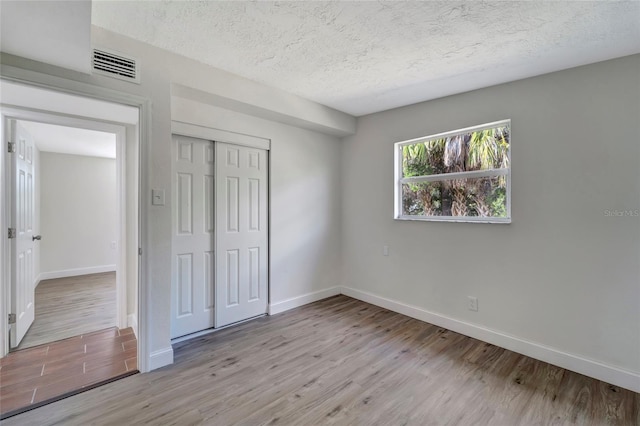 unfurnished bedroom featuring a textured ceiling, a closet, and light hardwood / wood-style flooring