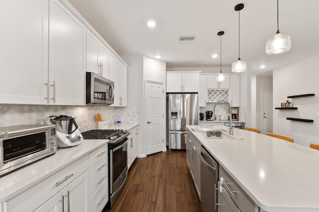 kitchen featuring decorative light fixtures, white cabinets, decorative backsplash, a kitchen island with sink, and stainless steel appliances