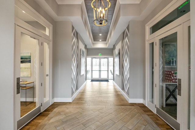 corridor with a raised ceiling, an inviting chandelier, and french doors