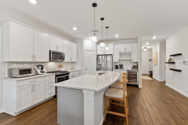 kitchen with pendant lighting, wine cooler, white cabinets, stainless steel appliances, and a center island with sink