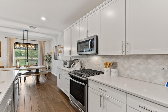 kitchen with white cabinetry, tasteful backsplash, decorative light fixtures, appliances with stainless steel finishes, and dark hardwood / wood-style floors