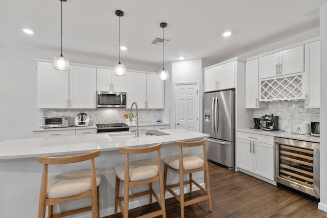 kitchen with white cabinets, appliances with stainless steel finishes, beverage cooler, and decorative light fixtures