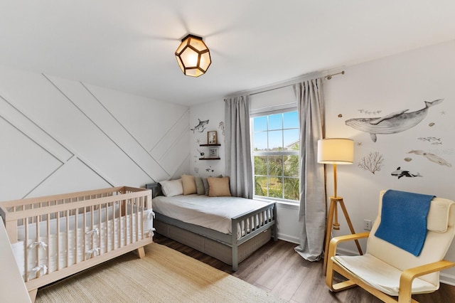 bedroom with wood-type flooring and a nursery area