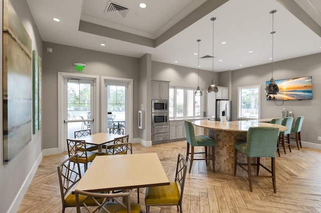 dining space featuring a raised ceiling, light parquet flooring, and ornamental molding