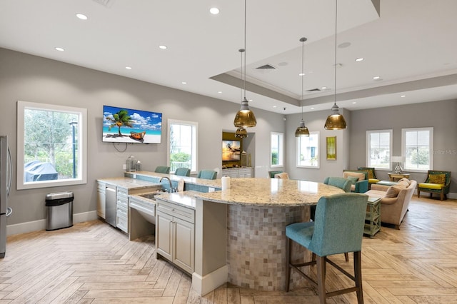 kitchen with a kitchen bar, stainless steel appliances, light stone counters, hanging light fixtures, and light parquet flooring