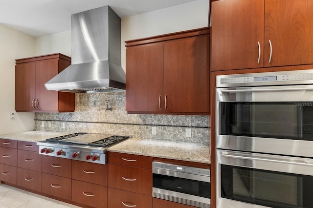 kitchen featuring appliances with stainless steel finishes, wall chimney exhaust hood, decorative backsplash, and light stone countertops