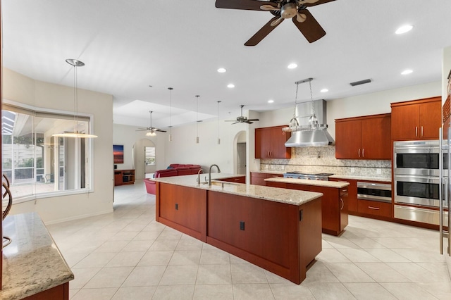 kitchen featuring tasteful backsplash, pendant lighting, sink, light stone countertops, and an island with sink