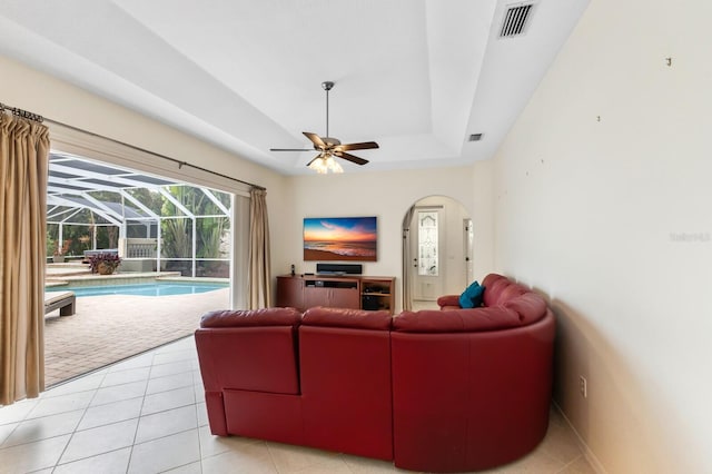 tiled living room with ceiling fan and a tray ceiling