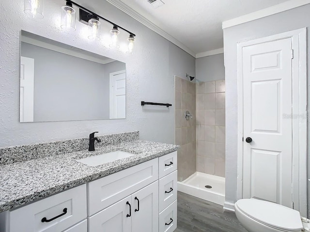 bathroom featuring toilet, vanity, tiled shower, wood-type flooring, and ornamental molding