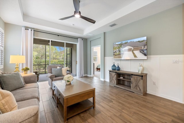 living room with a raised ceiling, hardwood / wood-style floors, and ceiling fan