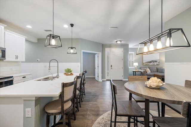 kitchen featuring visible vents, a sink, stainless steel microwave, dark wood-style floors, and light countertops