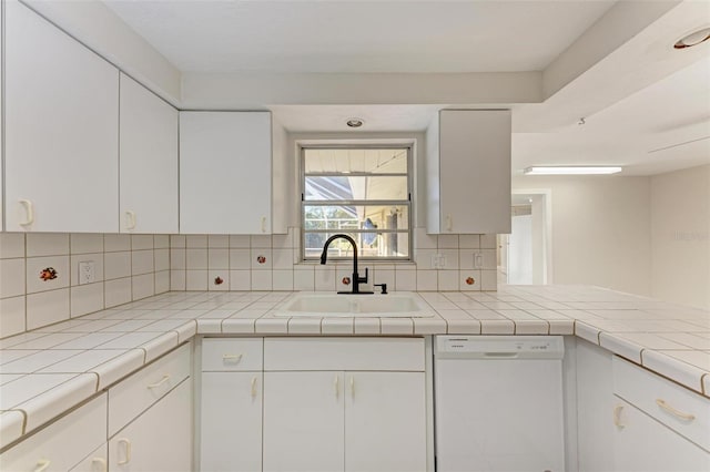 kitchen featuring backsplash, dishwasher, sink, white cabinetry, and tile counters