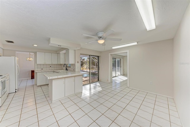 kitchen featuring backsplash, kitchen peninsula, sink, white cabinetry, and tile counters