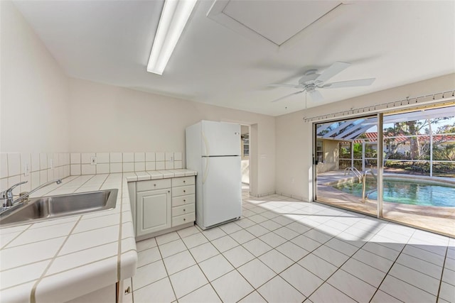 kitchen featuring white fridge, sink, tile countertops, light tile patterned flooring, and ceiling fan