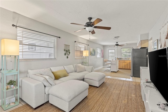 living area featuring light tile patterned floors, ceiling fan, visible vents, and baseboards