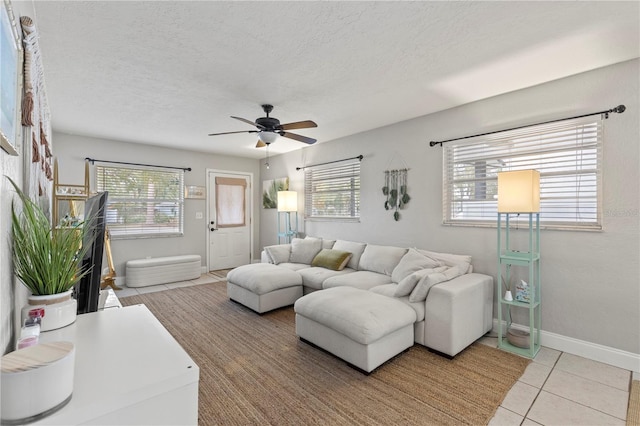 living area featuring light tile patterned floors, ceiling fan, a textured ceiling, and baseboards