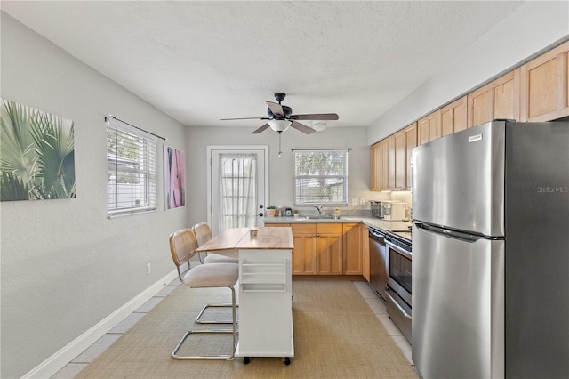 kitchen featuring a breakfast bar area, stainless steel appliances, a sink, light countertops, and light brown cabinetry