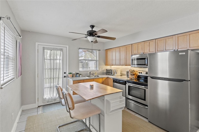 kitchen with light tile patterned floors, stainless steel appliances, light brown cabinetry, a ceiling fan, and a sink