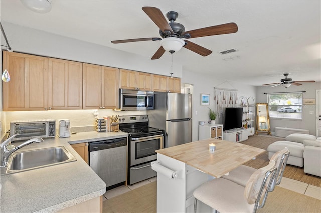 kitchen with appliances with stainless steel finishes, open floor plan, light countertops, light brown cabinets, and a sink