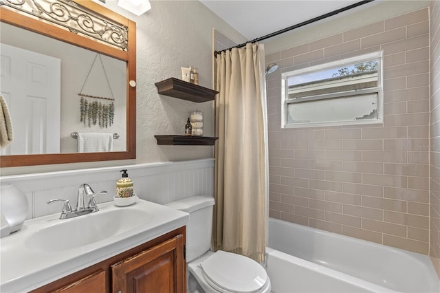 bathroom with a textured wall, toilet, wainscoting, shower / bathtub combination with curtain, and vanity