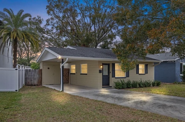 ranch-style house featuring concrete driveway, a front lawn, fence, and an attached carport