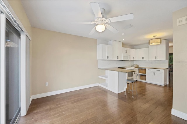 kitchen with kitchen peninsula, decorative backsplash, white appliances, a breakfast bar area, and white cabinets