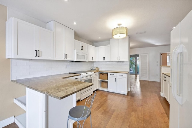 kitchen featuring white cabinetry, kitchen peninsula, white appliances, stone counters, and a breakfast bar