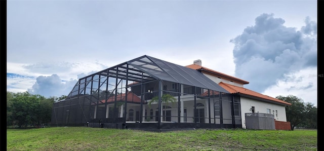 rear view of house with glass enclosure and a lawn