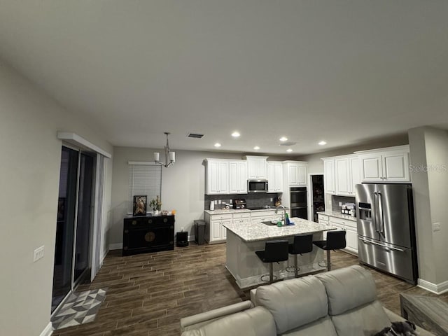 kitchen with white cabinetry, a center island with sink, stainless steel appliances, a kitchen breakfast bar, and pendant lighting