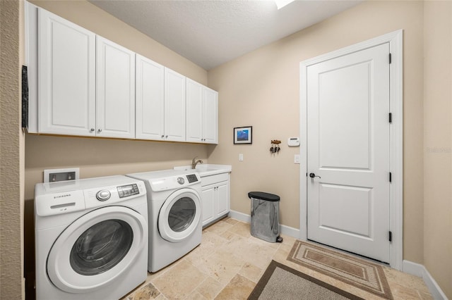 clothes washing area with cabinets, washing machine and dryer, sink, and a textured ceiling