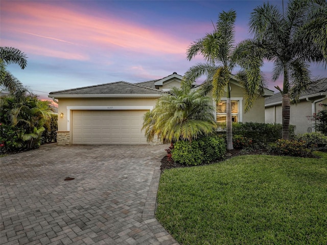 view of front of home featuring a garage, a yard, decorative driveway, and stucco siding