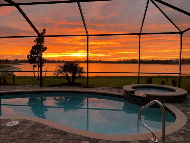 pool at dusk featuring a lanai, a water view, a patio, and an in ground hot tub