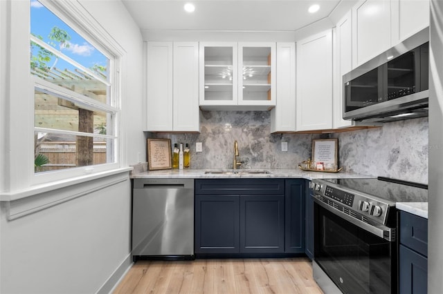 kitchen with light hardwood / wood-style floors, sink, light stone countertops, appliances with stainless steel finishes, and white cabinets