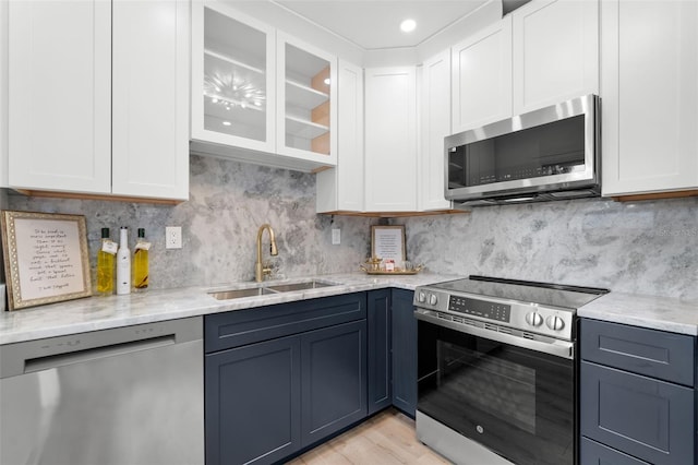 kitchen with light stone countertops, white cabinetry, stainless steel appliances, decorative backsplash, and sink