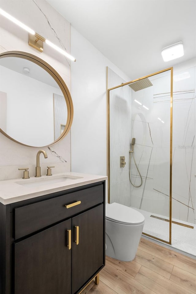 bathroom with toilet, vanity, wood-type flooring, and a tile shower