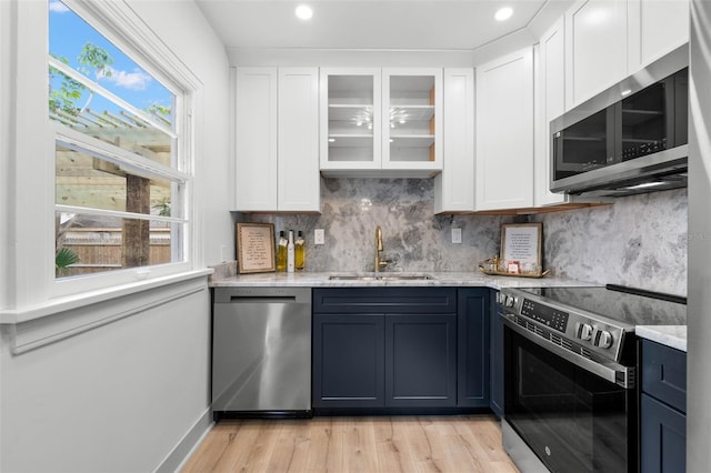 4536 1st Ave N, Saint Petersburg, FL 33713 - kitchen with light wood finished floors, stainless steel appliances, a sink, decorative backsplash, and white cabinetry
