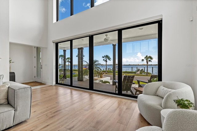 living room with a high ceiling, a water view, and light hardwood / wood-style flooring