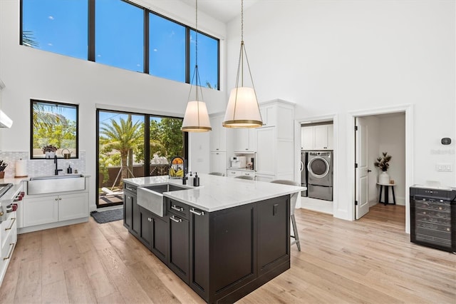 kitchen featuring hanging light fixtures, a kitchen island with sink, sink, and white cabinets