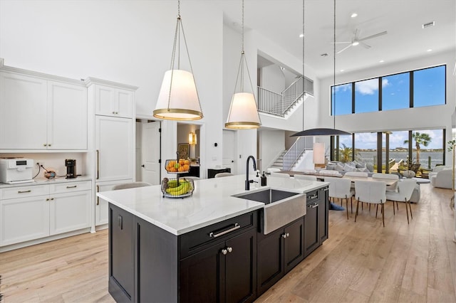 kitchen featuring sink, light hardwood / wood-style flooring, hanging light fixtures, a kitchen island with sink, and white cabinets