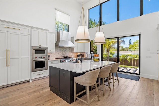 kitchen featuring white cabinetry, sink, a kitchen island with sink, light wood-type flooring, and wall chimney exhaust hood